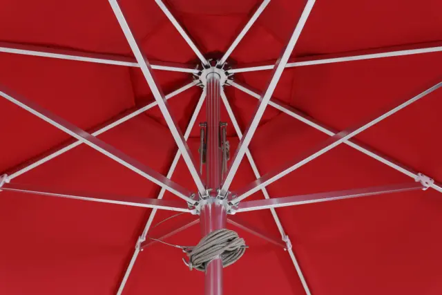 Detailed view from underneath the canopy of the red Bossa Nova center-pole market umbrella, showing the durable white aluminum frame, central hub, and rope pulley system.
