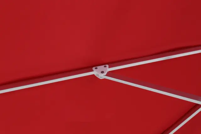 A detailed interior view of the red Bossa Nova center-pole market umbrella's canopy, showing the durable white hinged joint connecting the support arms to the main ribs of the frame.