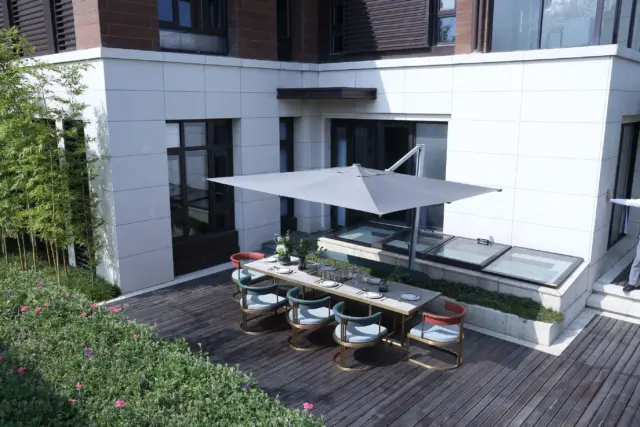 The large, grey Aman cantilever umbrella providing elegant shade for a modern outdoor dining set on a beautiful wooden patio next to a house.