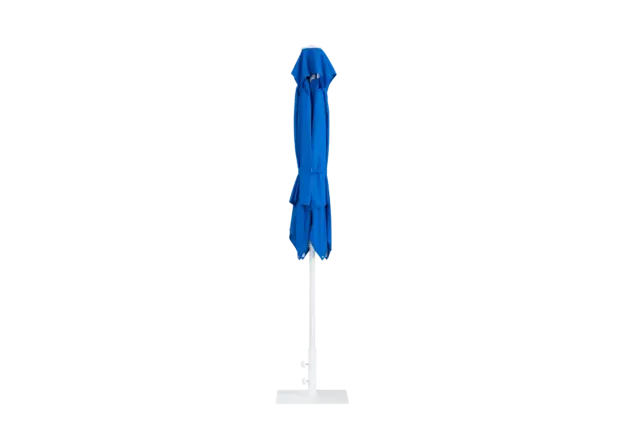 The blue Frappe center-pole umbrella in its closed position, neatly tied and standing upright on its white pole and base against a plain background.