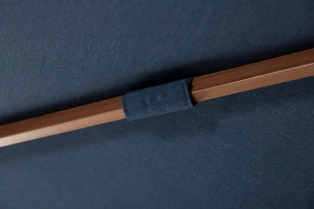 Detail view showing a navy fabric loop attaching the canopy to a wood-tone rib on the Piazza center pole umbrella.