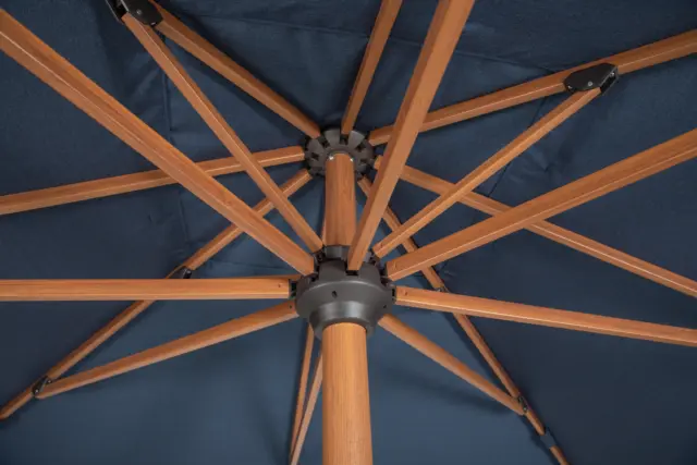 Underside view of an open Piazza center pole umbrella, showing the navy fabric canopy and the wood-tone frame ribs and central hub.