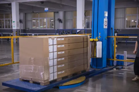 A pallet of finished products is securely wrapped by an automated stretch-wrapping machine in the factory's dispatch area, ensuring safe transit to customers worldwide.