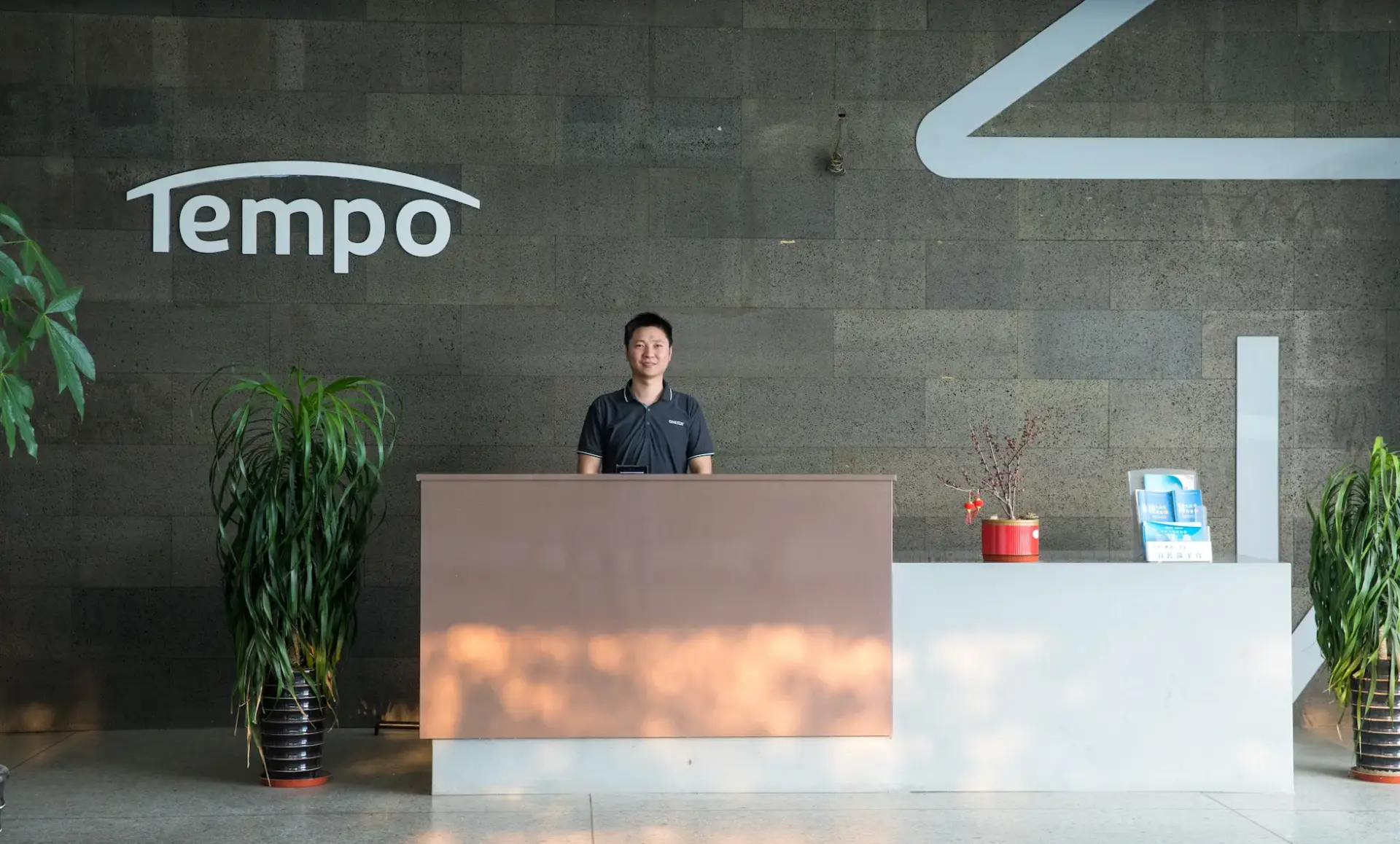The modern and welcoming reception lobby at the Tempo headquarters, with a friendly staff member smiling behind the front desk and the company logo on the wall.